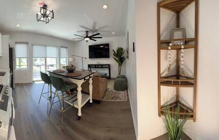 A spacious living area with a dining table, chairs, a ceiling fan, and a wooden shelving unit.