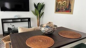 Une table à manger avec deux sets de table en fibres tressées, un bol de collations et un tableau accroché au mur.