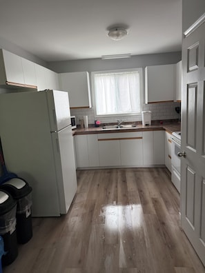 A kitchen with white cabinets, a refrigerator, a sink, and a window with curtains.