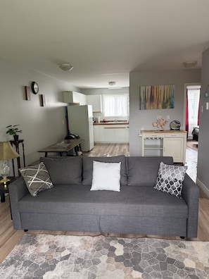 A living room with a grey sofa, a coffee table, a dining table, and a kitchen in the background.