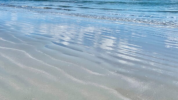Una playa con cielos despejados y olas suaves.