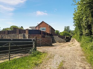 A gravel path leading to a brick building with a window and a metal gate.