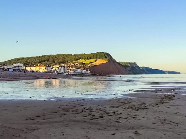 Un pueblo costero con edificios a lo largo de la playa, un acantilado y cielo despejado.