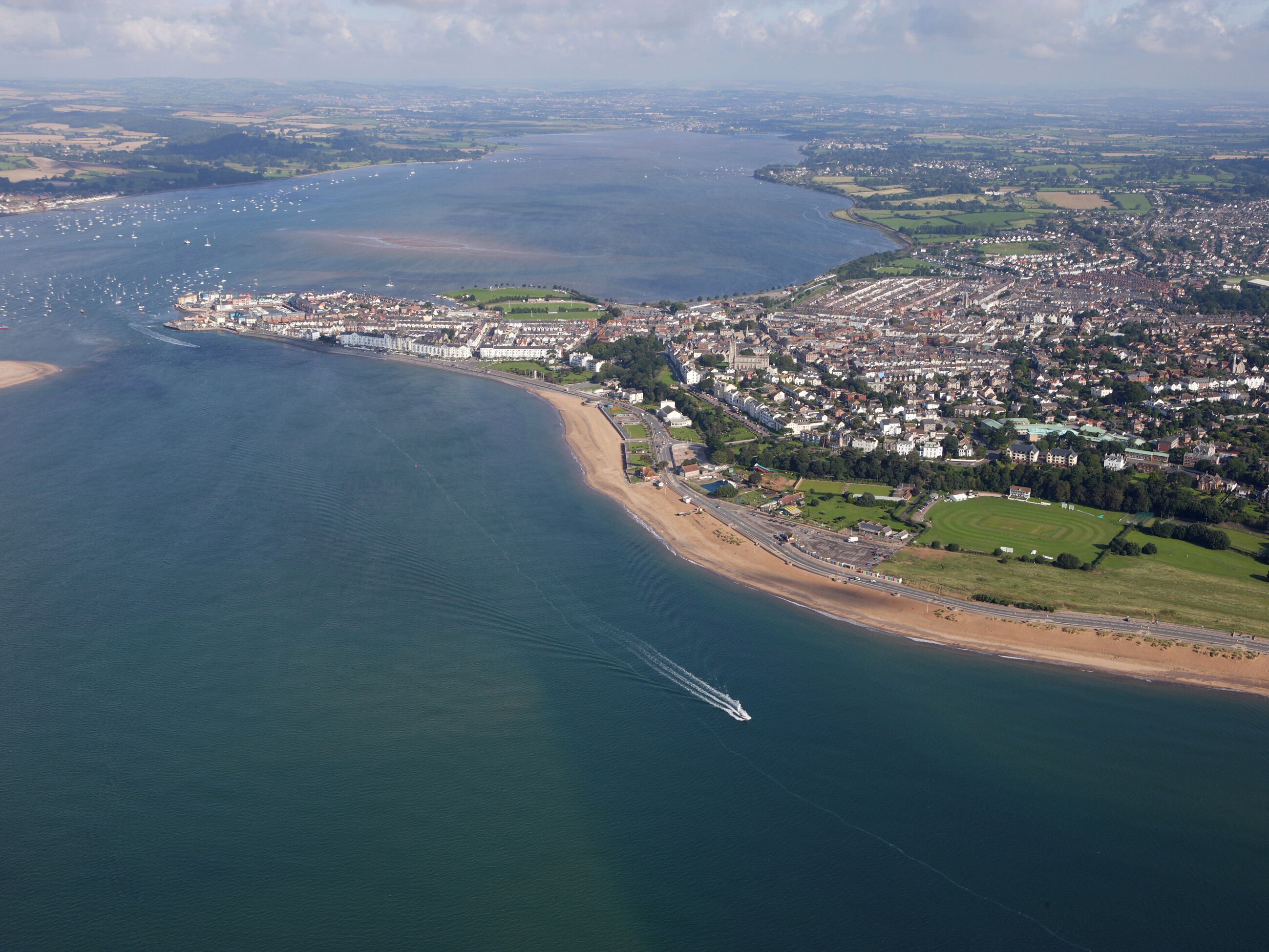 An aerial view of a coastal town with a beach, residential areas, and a marina.