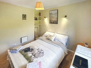 Un dormitorio con cama, mesita de noche, lámpara, decoración en la pared y un estante con artículos de aseo.
