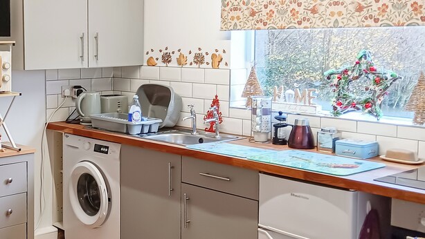 Una cocina con lavadora, un lavamanos y una ventana que da a árboles.