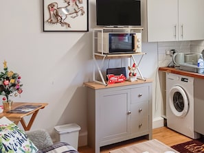 Una cocina compacta con microondas, lavadora y una pequeña mesa con una computadora portátil.