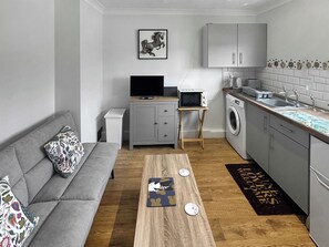 Un espacio habitable compacto con sofá, mesa de centro, televisión, microondas, lavadora y pequeña mesa de comedor.