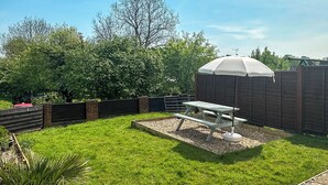 Un patio trasero con una mesa de picnic, una valla de madera y un árbol.