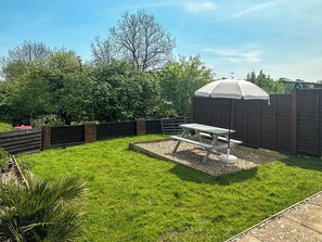 Un jardin avec une table de pique-nique, une clôture en bois et un arbre.