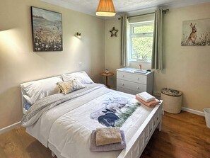 Une chambre à coucher avec un lit, une table de chevet, une fenêtre et un mur orné d’un tableau.