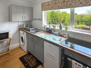 Cocina compacta con lavadora, microondas, fregadero y ventana con vistas al verdor.