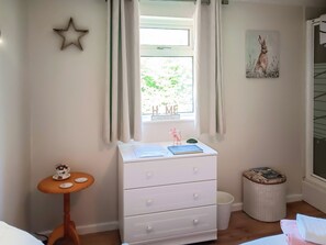 Un dormitorio con ventana, cómoda, mesita y un cuadro en la pared.