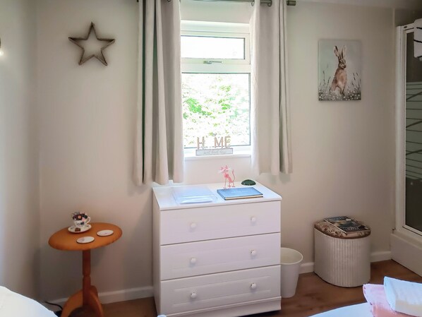 Un dormitorio con ventana, cómoda, mesita y un cuadro en la pared.