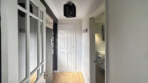 Un pasillo con suelo de madera, una puerta blanca y un candelabro colgante.