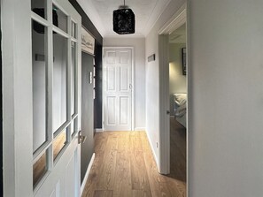 Un pasillo con suelo de madera, una puerta blanca y un candelabro colgante.