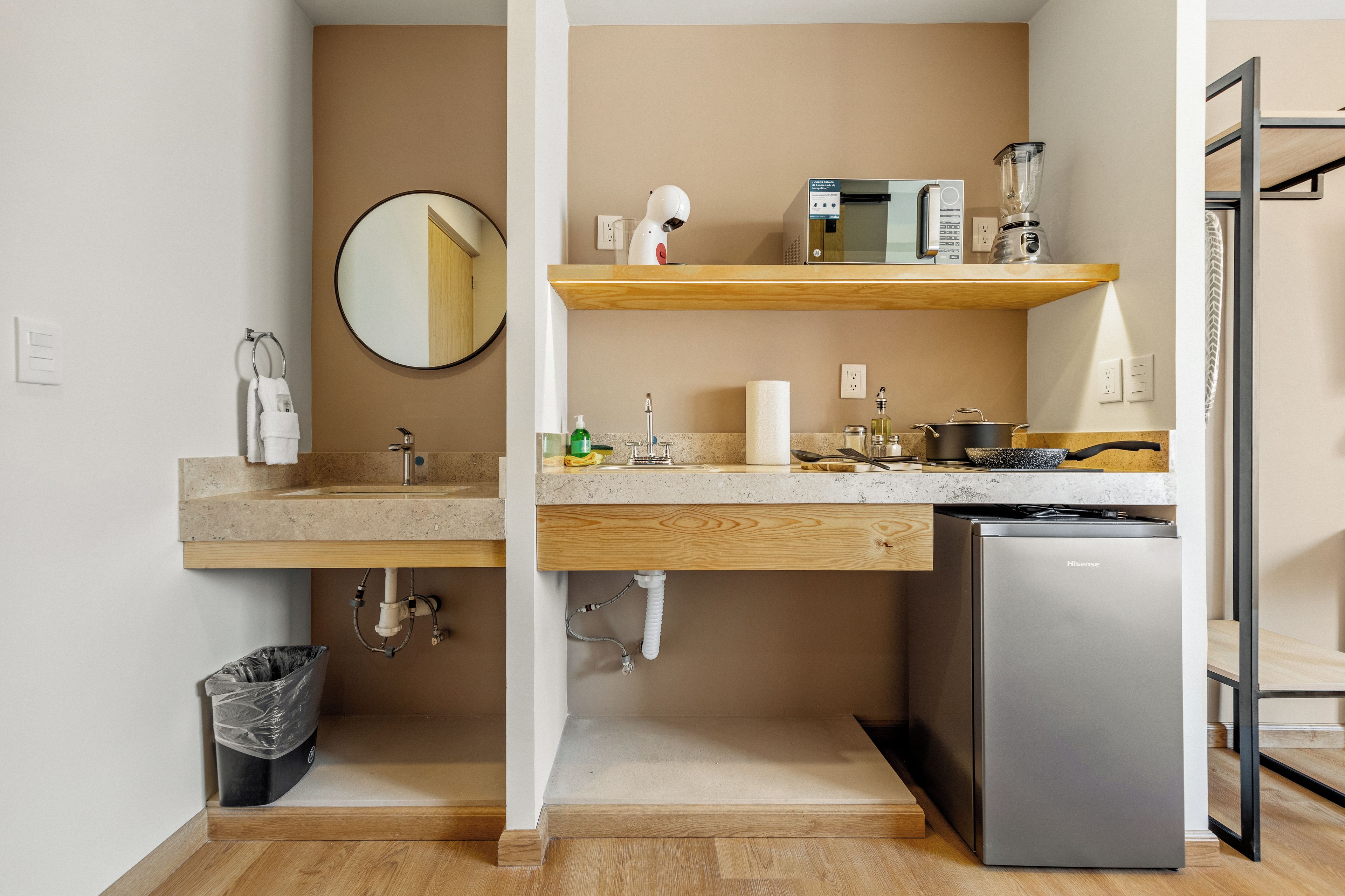 Una cocina compacta con un lavamanos, microondas, licuadora y un refrigerador pequeño.
