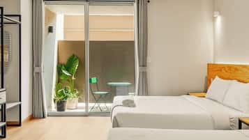 Une chambre d’hôtel avec deux lits, un ventilateur de plafond, une vue sur le balcon extérieur et une plante en pot.