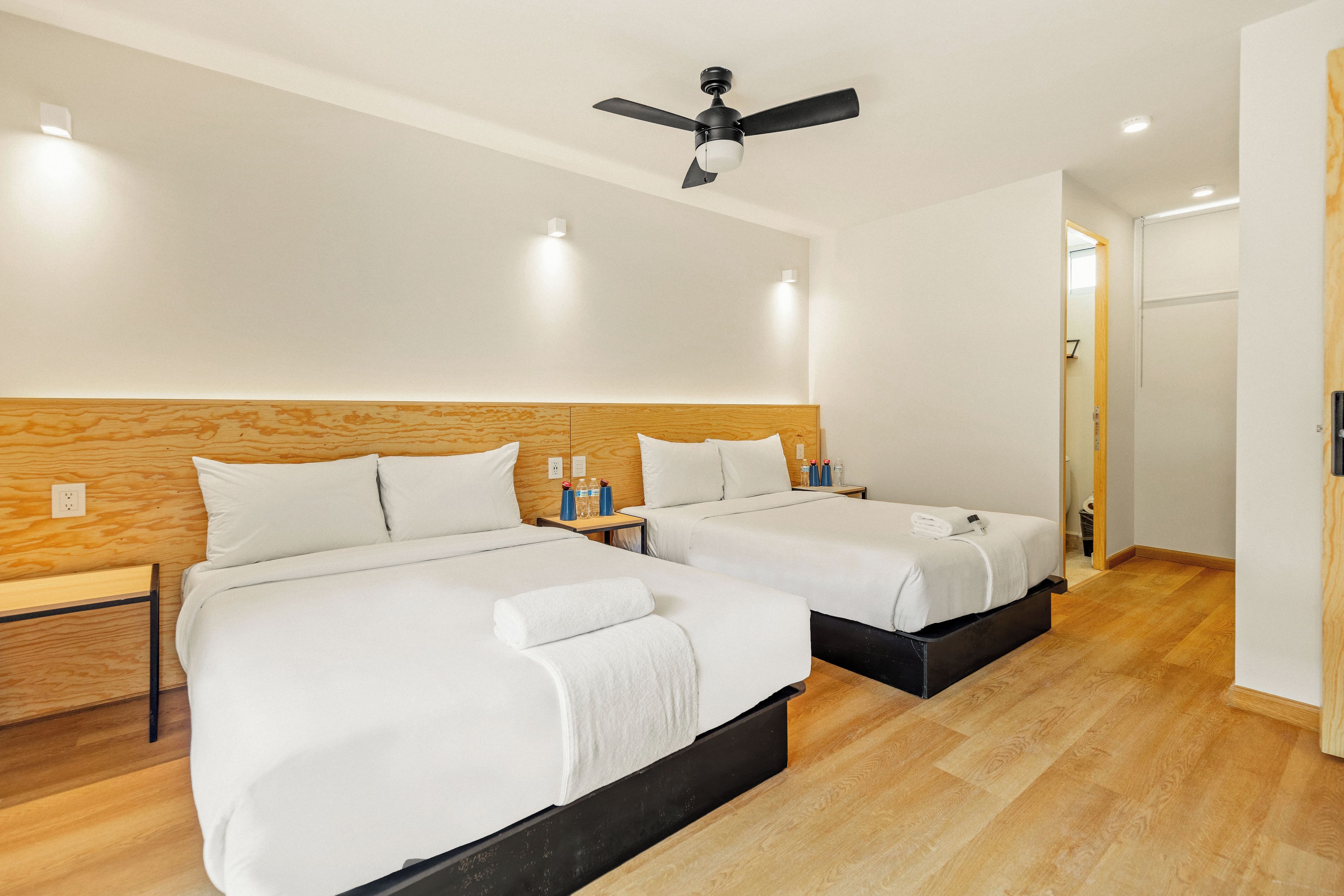 A hotel room with two beds, wooden headboards, a ceiling fan, and a door leading to another room.