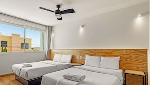 Hotelkamer met twee bedden, een plafondventilator, een raam met uitzicht op gebouwen en een houten hoofdeinde.