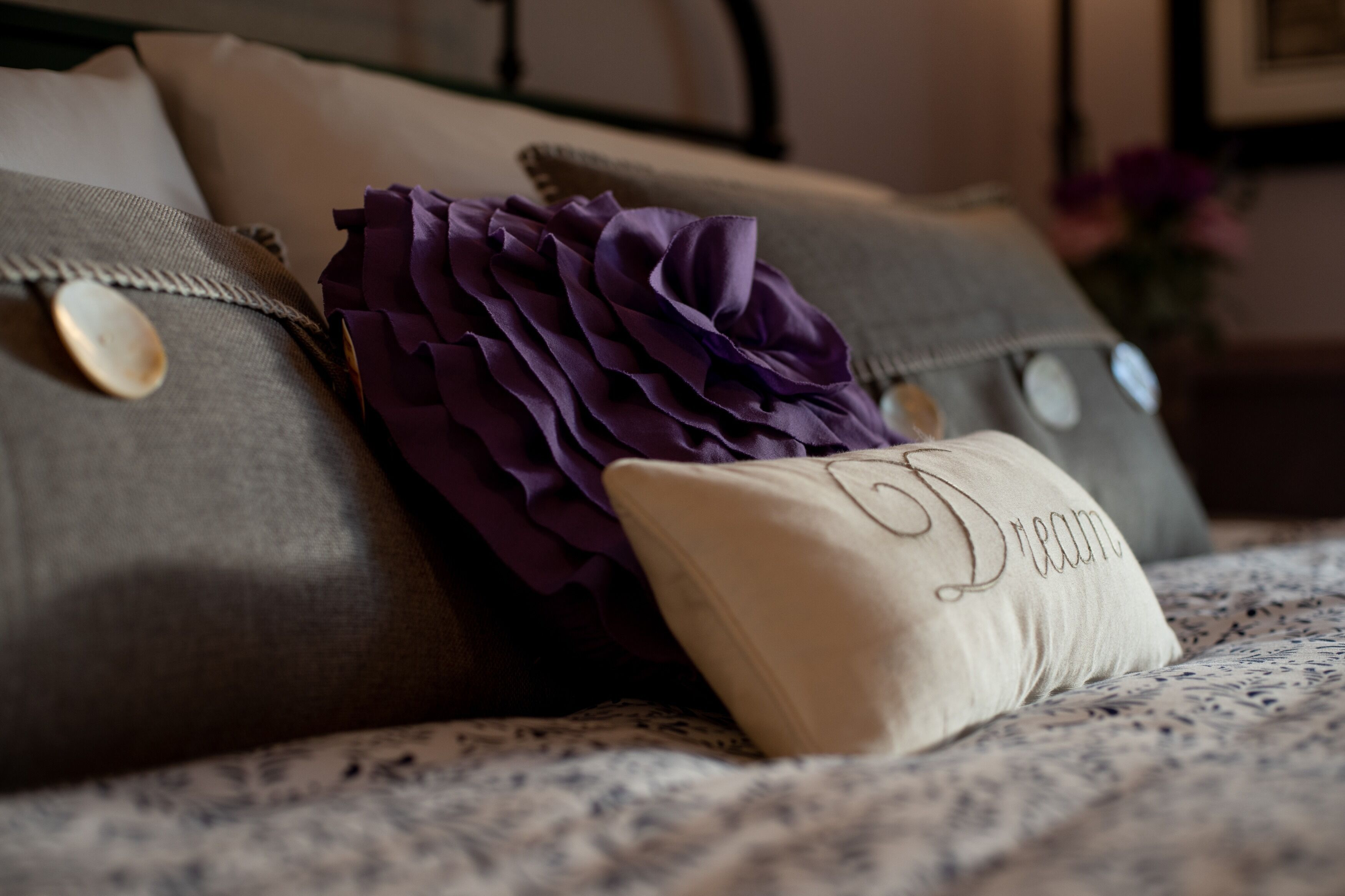 A bed with a patterned bedspread, a decorative purple pillow, and a pillow with the name "Diana" embroidered on it.