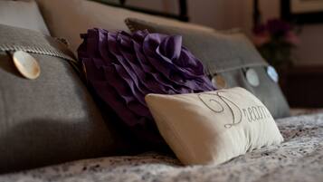 A bed with a patterned bedspread, a decorative purple pillow, and a pillow with the name "Diana" embroidered on it.