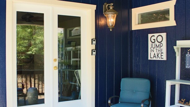 A blue wooden exterior with a white door, a teal chair, and a 'GO JUMP IN THE LAKE' sign. - Drakeslanding Inn (Shaver Lake)