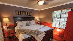 A bedroom with a large bed, a nightstand, a dresser, and a window with blinds. - Drakeslanding Inn (Shaver Lake)