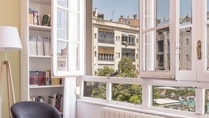 A room with a large window, a bookshelf, a chair, and a table. - Bright and Quiet Duplex Apartment (Barcelona)