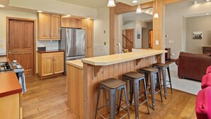 Una cocina moderna con armarios de madera, un refrigerador de acero inoxidable y una zona de bar con taburetes.