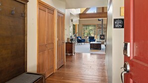 Un pasillo con pisos de madera y puertas que conduce a una sala de estar con chimenea y asientos.