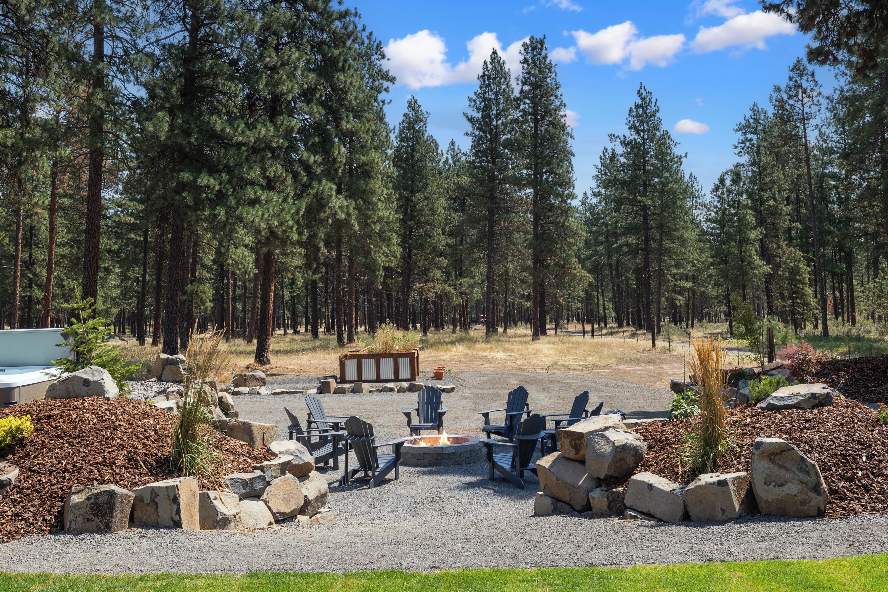 A campground with a fire pit, seating area, and surrounding trees.