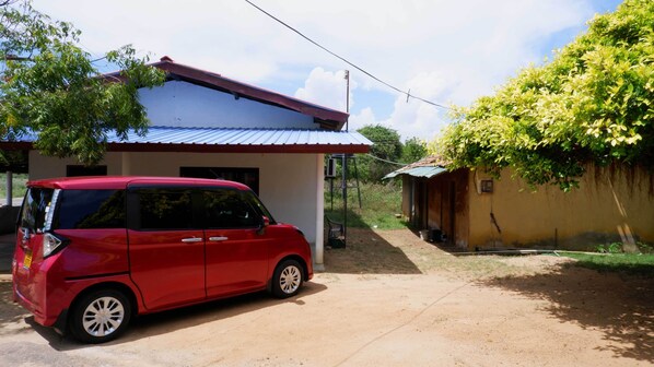 A red car parked in front of a house with a red roof and a small shed nearby. - Attale Resort (Bundala)