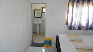A room with a bed, a bedside table, a window with curtains, a sink, and a door leading to another room. - Attale Resort (Bundala)