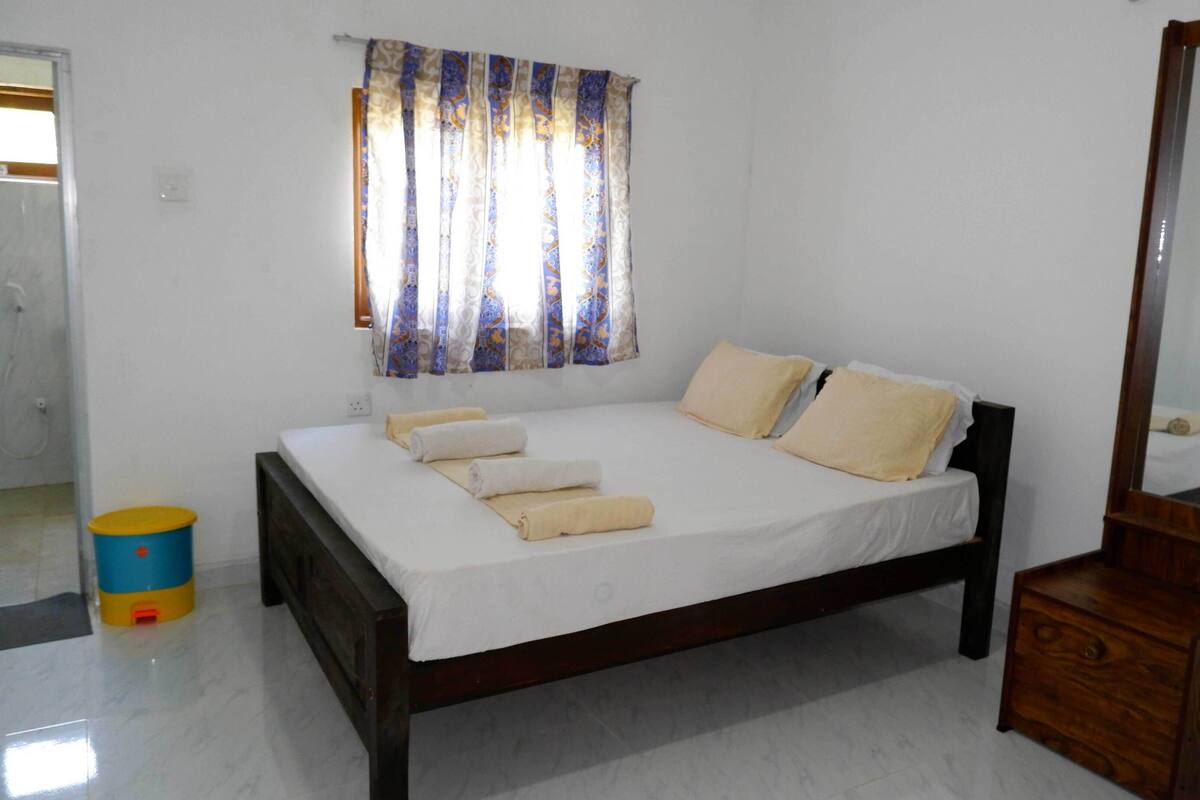 Un dormitorio con cama, cómoda de madera, espejo y ventana con cortinas estampadas.
