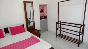 A bedroom with a bed, a wooden dresser, a mirror, a metal rack, and a door with a sunset painting. - Attale Resort (Bundala)