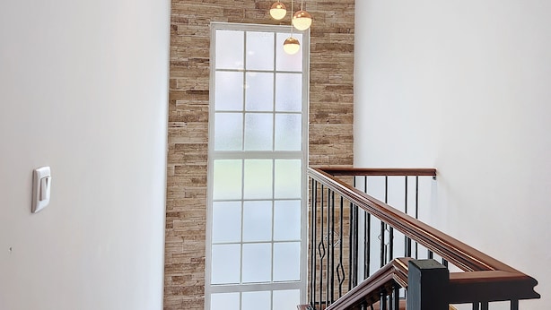 Una escalera con barandilla de madera y pared de piedra, con una puerta de cristal grande y satinado.