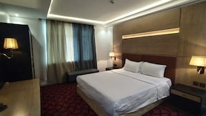 A hotel room with a large bed, a desk, a chair, a TV, and a window with curtains. - Jeddah Grand Beach (Jeddah)