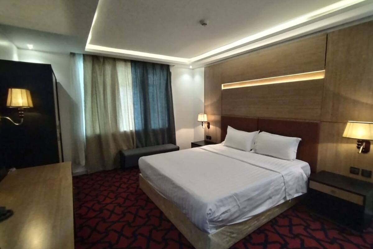 A hotel room with a large bed, a desk, a chair, a TV, and a window with curtains.