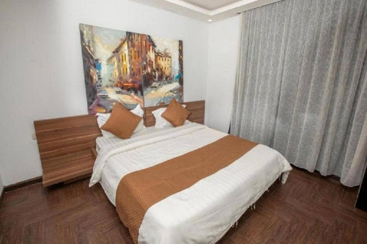 A hotel room with a large bed, wooden headboard, and a painting above it.