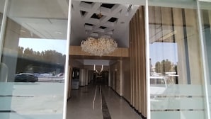 A modern hotel lobby with a central chandelier, a glass wall, and a view of parked cars outside. - Jeddah Grand Beach (Jeddah)