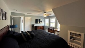 Ein Schlafzimmer mit Bett, Schreibtisch, Stuhl, Deckenventilator und Kamin.