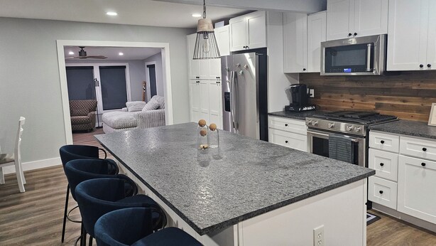 Una cocina moderna con armarios blancos, encimera de granito y refrigerador de acero inoxidable.