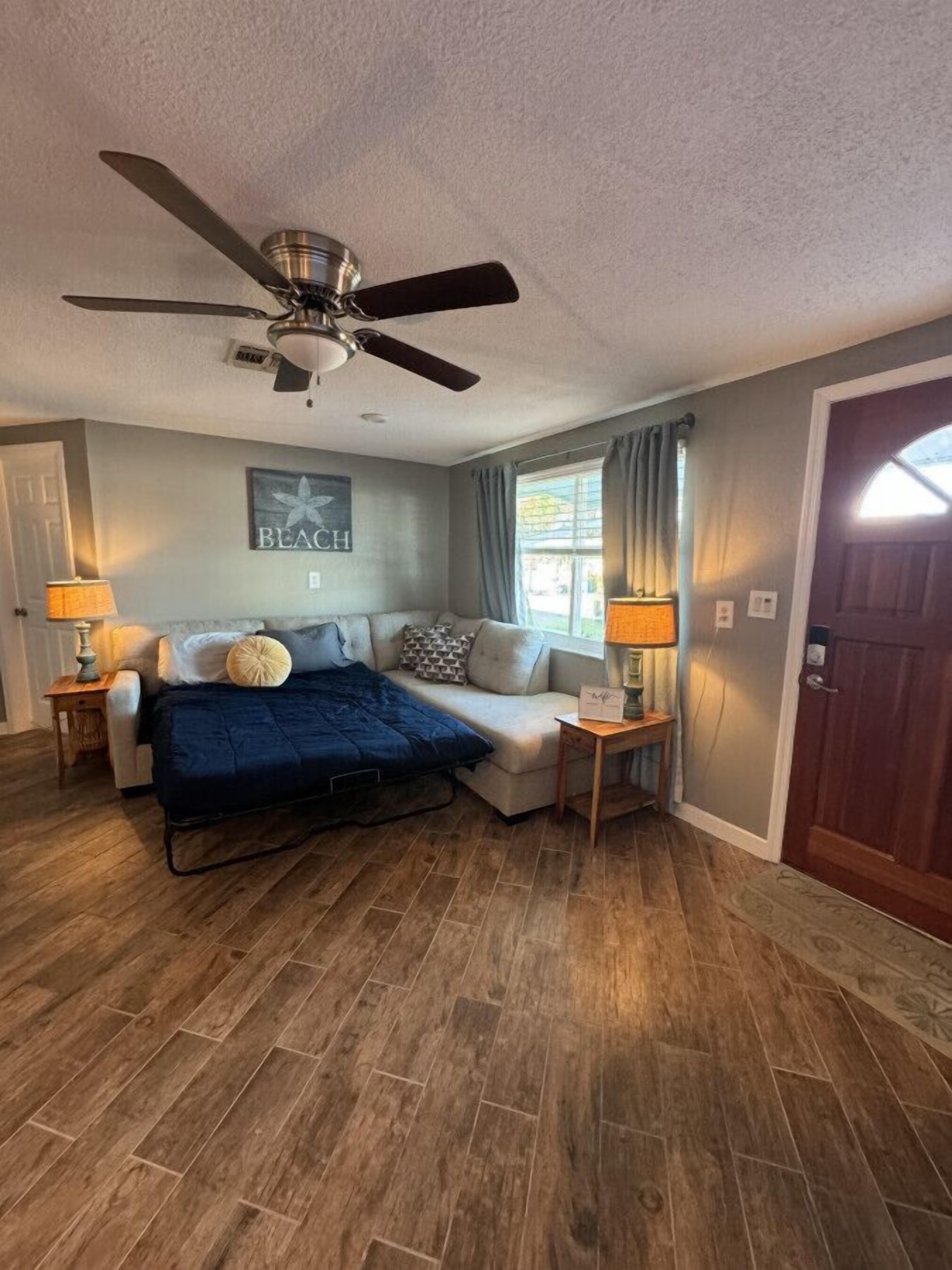 A bedroom with a bed, a ceiling fan, a window with curtains, and a door.