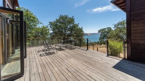 Een houten terras met buitenmeubilair, met uitzicht op water en bomen.