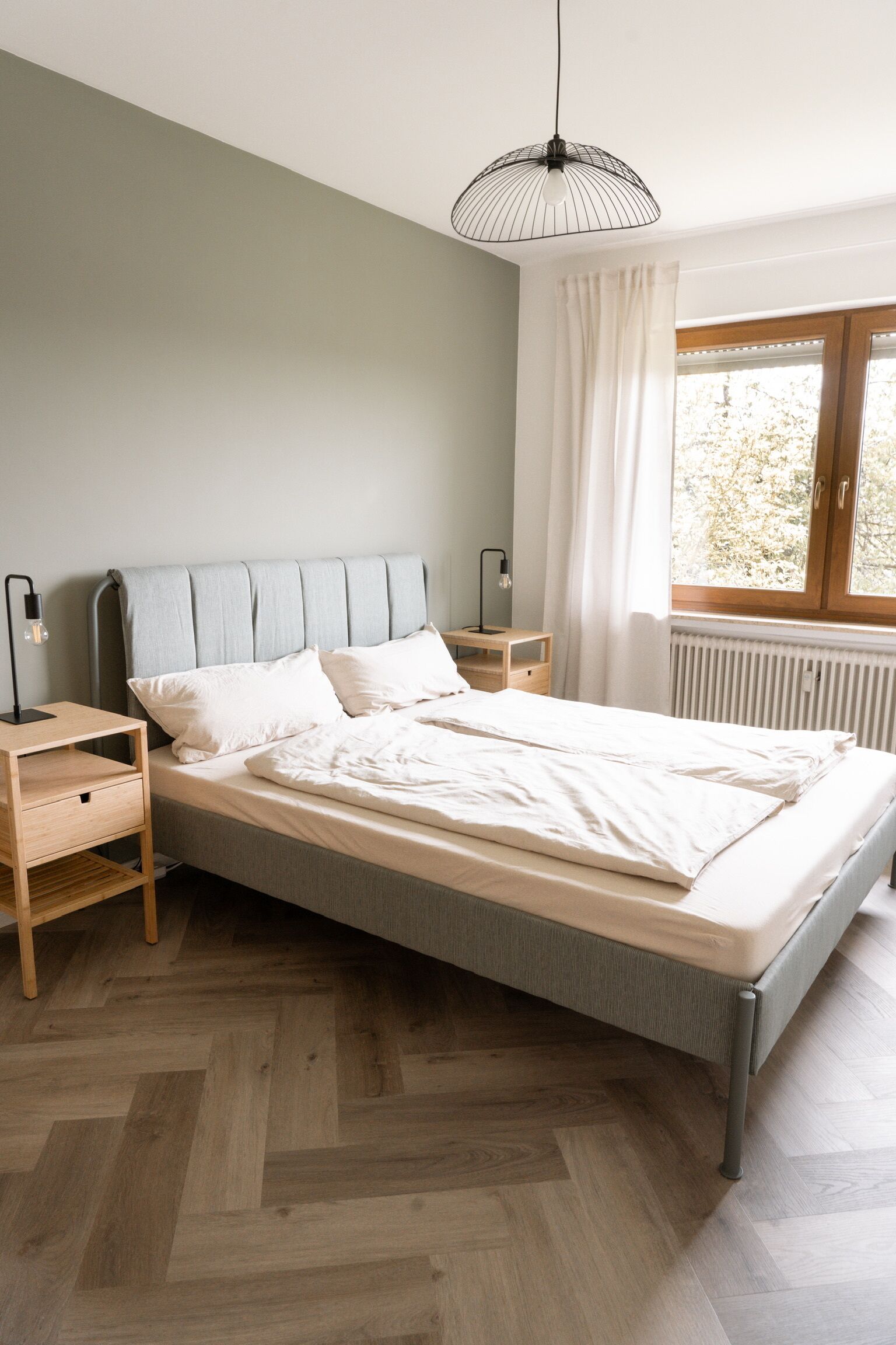 Ein Schlafzimmer mit Bett, Nachttischen, einem Fenster mit Vorhängen und einer Heizung.