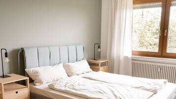 Ein Schlafzimmer mit Bett, Nachttischen, einem Fenster mit Vorhängen und einer Heizung.