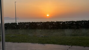 Vista del atardecer desde un balcón con piso de madera y barandilla de metal.