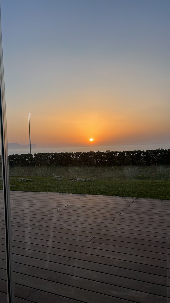 A sunset view from a balcony with a wooden floor and a metal railing.