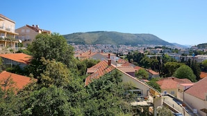 A residential area with red-tiled roofs, surrounded by greenery, and a distant view of a hill with buildings. - A3 KABLAR'S SUNNY SUITES 1BR APT with balcony and sea view - Duplicate (Dubrovnik)